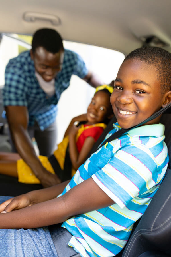 A father buckling his children's seatbelts inside their car in Farmington Hills, MI, symbolizing complete protection with AAA life insurance policies at Mark Ismail Insurance Agency.